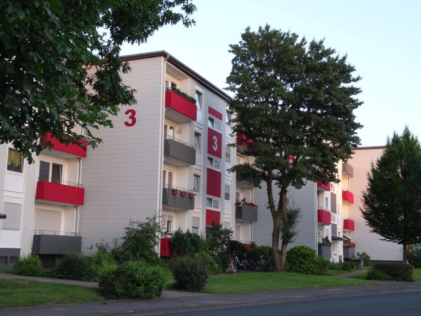 Fassade Mehrfamilienhaus mit Vorgärten und roten Balkonen