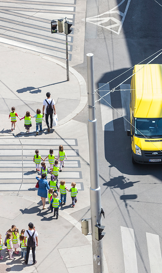 Kinder mit gelben Warnwesten laufen über Straßenkreuzung mit Zebrastreifen